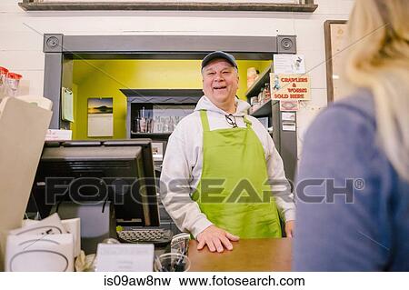 Stock Photo - Owner in general store serving customer at counter. Fotosearch