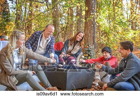 Stock Image - Parents with adult and teenage children toasting marshmallows in woods. Fotosearch