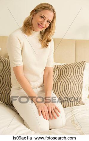 Stock Image - Portrait blond mature woman kneeling on bed. Fotosearch