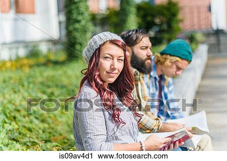 Stock Image - Portrait of adult college students reading books on campus wall. Fotosearch