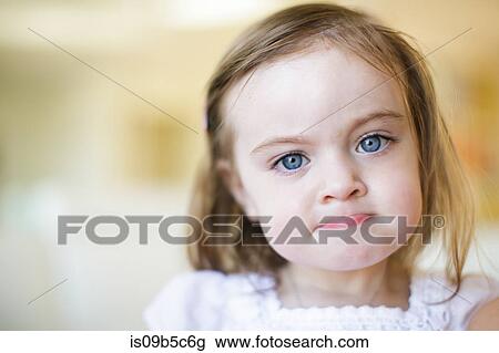 Stock Image - Portrait of blue eyed female toddler biting lip. Fotosearch