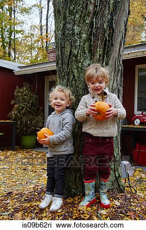 Portrait of boy and male toddler leaning against garden tree holding pumpkins View Large Photo Image Stock Image - Portrait of boy and male toddler leaning against garden tree holding pumpkins. Fotosearch