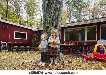 Portrait of boy and male toddler leaning against garden tree holding pumpkins View Large Photo Image Stock Image - Portrait of boy and male toddler leaning against garden tree holding pumpkins. Fotosearch