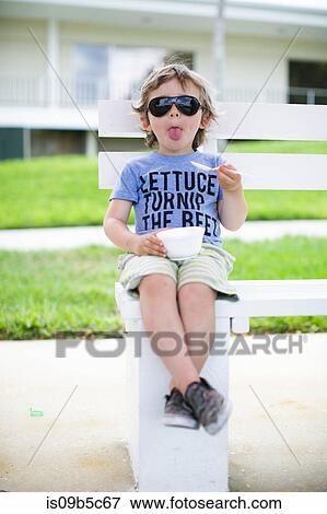 Stock Photo - Portrait of boy sitting on bench eating bowl of ice cream. Fotosearch