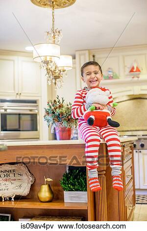 Stock Photo - Portrait of boy sitting on kitchen counter holding santa toy. Fotosearch