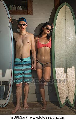 Stock Photo - Portrait of cool young surfing couple standing on porch, Rockaway Beach, New York State, USA. Fotosearch