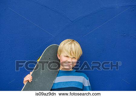 Portrait of cute boy carrying skateboard on shoulder in front of blue wall View Large Photo Image Picture - Portrait of cute boy carrying skateboard on shoulder in front of blue wall. Fotosearch