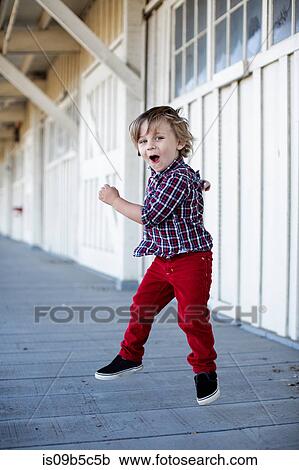 Stock Image - Portrait of cute boy jumping mid air on porch. Fotosearch