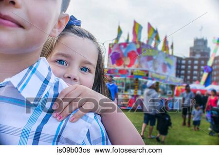 Portrait of cute girl peering from brothers shoulder at amusement park View Large Photo Image Stock Photograph - Portrait of cute girl peering from brothers shoulder at amusement park. Fotosearch