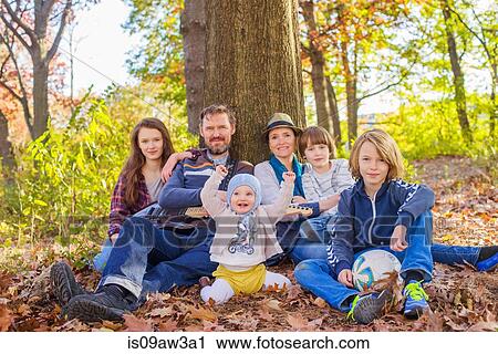 Stock Image - Portrait of family sitting in forest, beside tree. Fotosearch