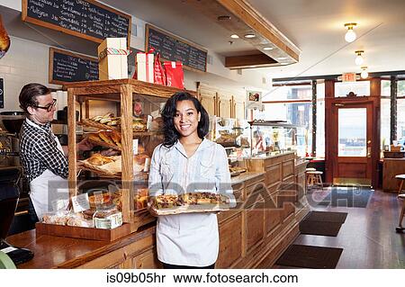 Stock Photography - Portrait of female worker in bakery holding fresh pastries. Fotosearch