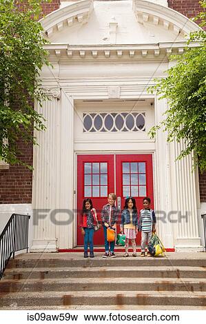 Stock Photo - Portrait of four boys and girls standing elementary school entrance. Fotosearch