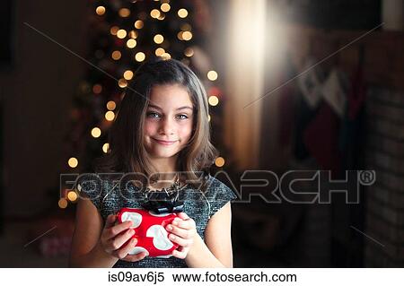 Portrait of girl in front of christmas tree holding gift looking at camera smiling View Large Photo Image Stock Photography - Portrait of girl in front of christmas tree holding gift looking at camera smiling. Fotosearch