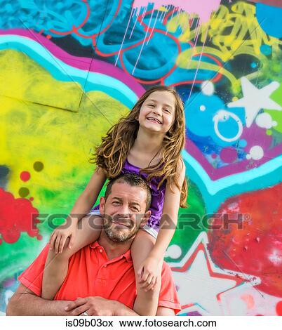 Stock Photo - Portrait of girl on father's shoulders in front of wall mural at amusement park. Fotosearch