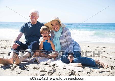 Stock Image - Portrait of grandparents and grandson, sitting on beach, smiling. Fotosearch