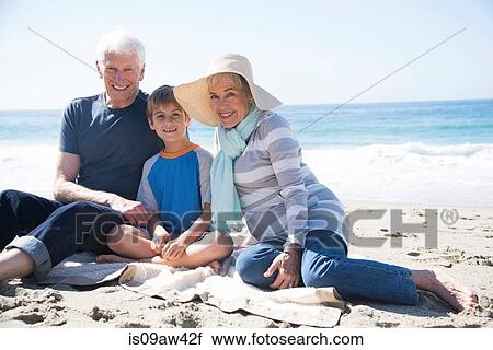 Stock Image - Portrait of grandparents and grandson, sitting on beach, smiling. Fotosearch