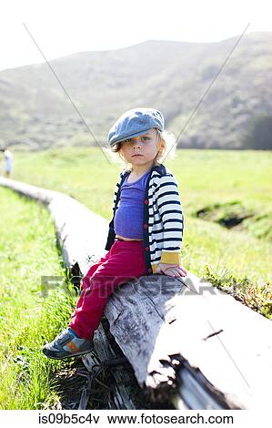 Stock Photo - Portrait of male toddler in flat cap sitting on log. Fotosearch