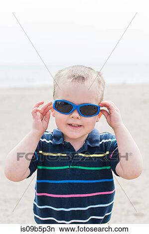 Portrait of male toddler putting on blue sunglasses at beach View Large Photo Image Picture - Portrait of male toddler putting on blue sunglasses at beach. Fotosearch