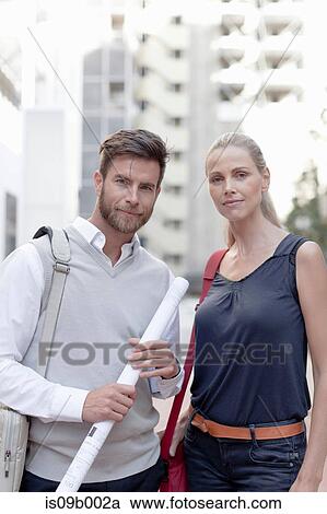 Stock Image - Portrait of man and woman outdoors, man holding rolled up documents. Fotosearch