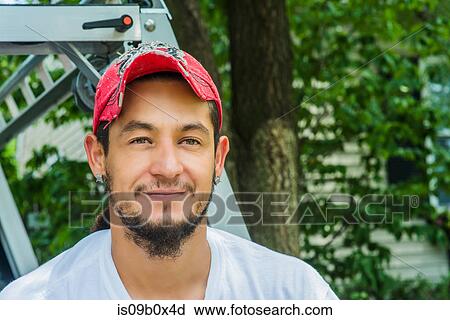 Stock Image - Portrait of man wearing baseball cap looking at camera smiling. Fotosearch