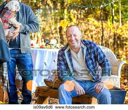 Stock Photograph - Portrait of mature man sitting in woods with adult son and dog. Fotosearch