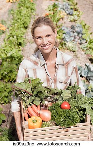Stock Image - Portrait of mature woman in garden, holding crate of fresh vegetables. Fotosearch