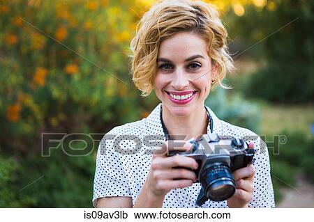 Portrait of mid adult woman holding SLR camera, smiling View Large Photo Image Stock Image - Portrait of mid adult woman holding SLR camera, smiling. Fotosearch