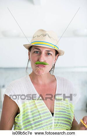 Stock Image - Portrait of mid adult woman in straw hat and pea pod moustache. Fotosearch