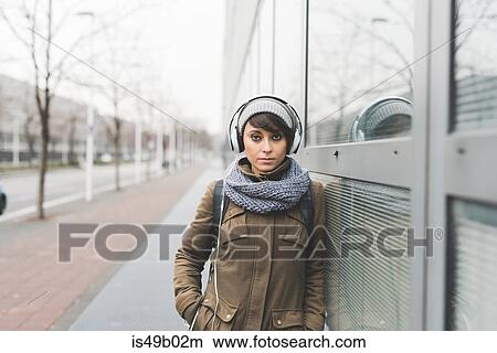 Portrait of mid adult woman listening to headphones and leaning against city office block View Large Photo Image Picture - Portrait of mid adult woman listening to headphones and leaning against city office block. Fotosearch