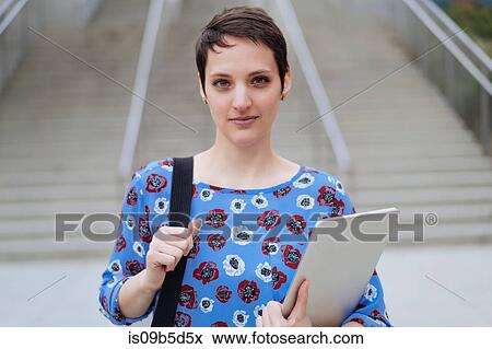 Portrait of mid adult woman standing outdoors, holding bag and laptop View Large Photo Image Stock Photo - Portrait of mid adult woman standing outdoors, holding bag and laptop. Fotosearch