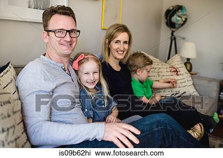Stock Image - Portrait of parents sitting on sofa with daughter and son. Fotosearch