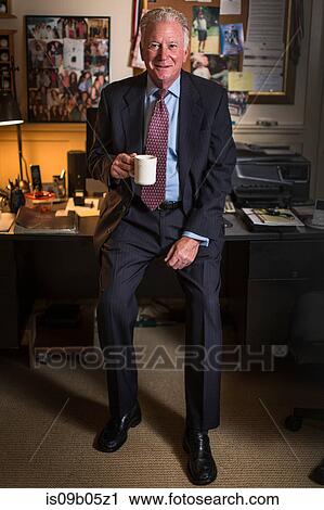 Stock Image - Portrait of senior businessman sitting on office desk. Fotosearch