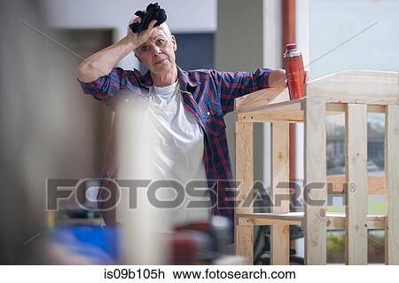 Stock Image - Portrait of senior female carpenter with hand on forehead in furniture making workshop. Fotosearch
