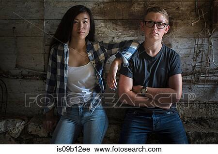 Stock Image - Portrait of sullen teenage couple leaning against dusty shed wall. Fotosearch