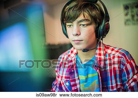 Portrait of teenage boy sitting at desk using computer wearing headset View Large Photo Image Stock Photography - Portrait of teenage boy sitting at desk using computer wearing headset. Fotosearch