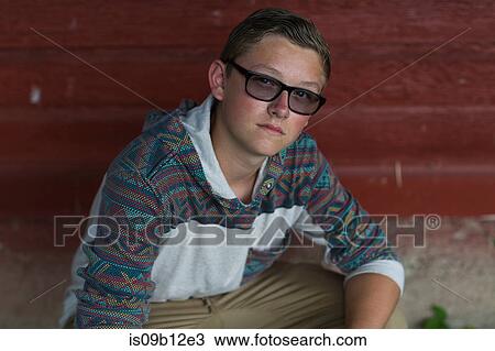 Stock Image - Portrait of teenage boy wearing tinted eyeglasses crouching in porch. Fotosearch