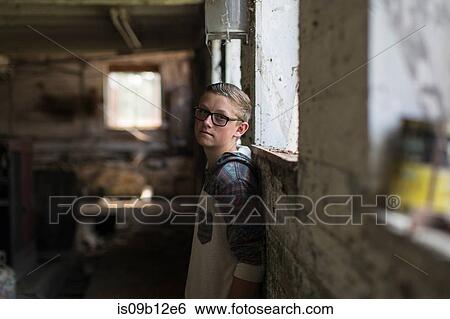 Stock Photograph - Portrait of teenage boy wearing tinted eyeglasses leaning against shed wall. Fotosearch