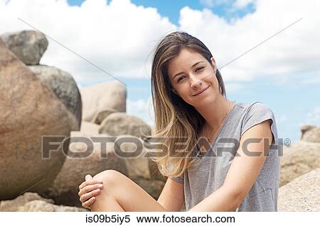 Stock Photography - Portrait of teenage girl sitting on rocks looking at camera smiling. Fotosearch