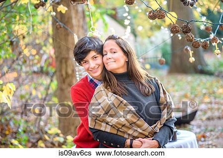 Stock Photograph - Portrait of teenage son hugging mother in woods. Fotosearch