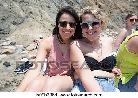 Stock Image - Portrait of two friends sitting on beach, smiling, Block Island, Rhode Island, USA. Fotosearch