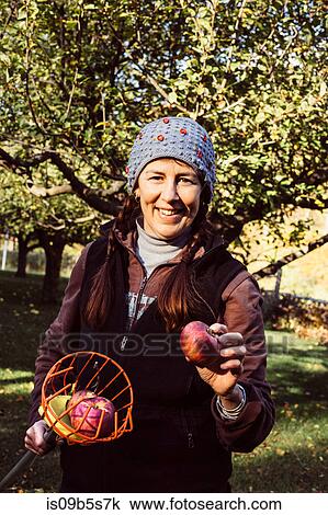 Stock Image - Portrait of woman holding fruit picker and fresh apple. Fotosearch