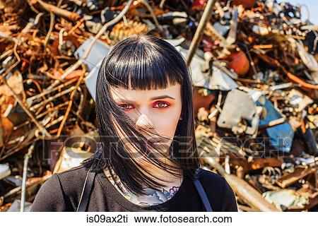 Stock Image - Portrait of woman in scrap yard looking at camera. Fotosearch