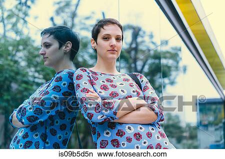Picture - Portrait of woman leaning against mirrored window, arms folded. Fotosearch