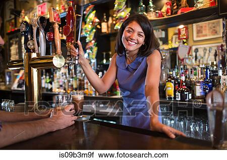 Stock Image - Portrait of young female barmaid serving beer in public house. Fotosearch