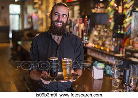 Portrait of young male bartender carrying tray of beer in public house View Large Photo Image Stock Image - Portrait of young male bartender carrying tray of beer in public house. Fotosearch