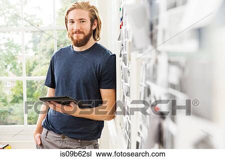 Stock Image - Portrait of young male designer leaning against mood board in creative studio. Fotosearch