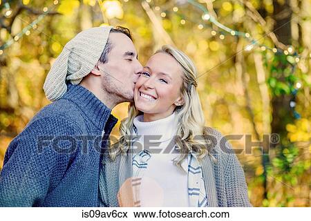 Portrait of young man kissing young woman on cheek in woods View Large Photo Image Stock Photo - Portrait of young man kissing young woman on cheek in woods. Fotosearch