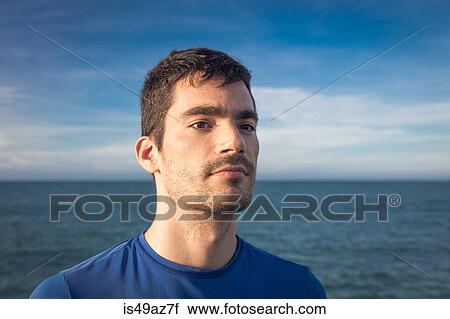 Stock Image - Portrait of young man outdoors, near water, looking away. Fotosearch