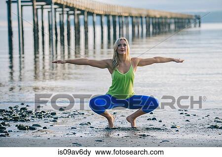 Stock Photo - Portrait of young woman crouching in yoga pose on beach. Fotosearch