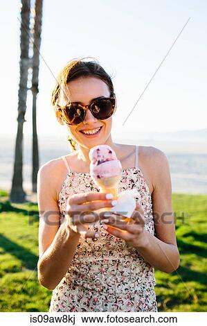 Stock Image - Portrait of young woman eating ice cream cone at coast, Venice Beach, California, USA. Fotosearch
